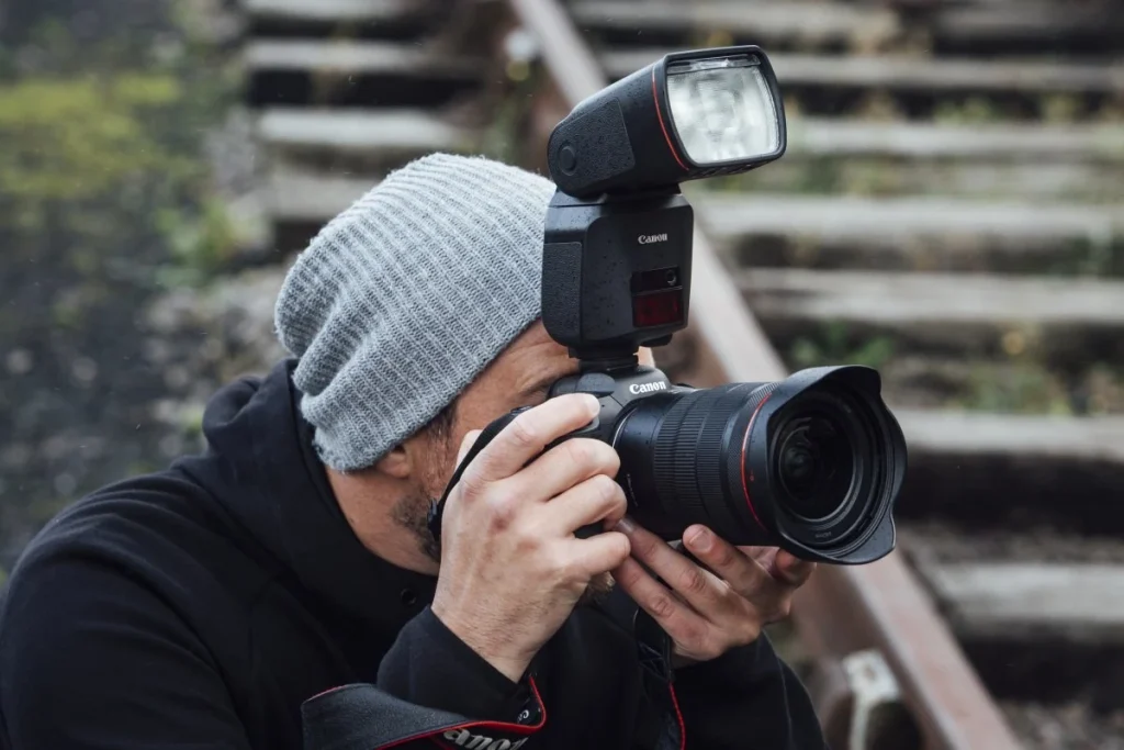 Фотограф веде репортажну зйомку на камеру Canon EOS R зі спалахом Canon Speedlite EL-1 під час дощу на відкритому стадіоні